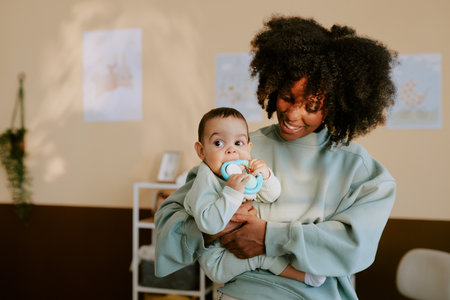 African American mom holding her male child while he biting blue rattleの写真素材