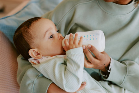 Medium close up of caring female hands holding her son and bottle with formula to feed babyの写真素材