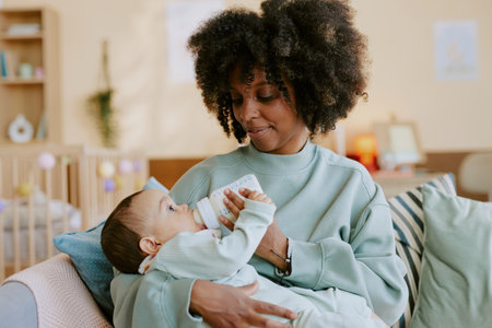 African American mother holding her son and feeding him formula while baby trying to hold bottle by himselfの写真素材