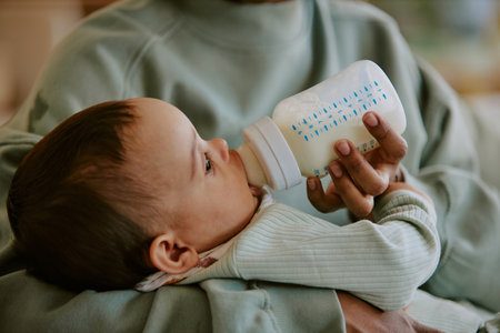 Medium close up of baby boy eating formula while his mother helping him with it