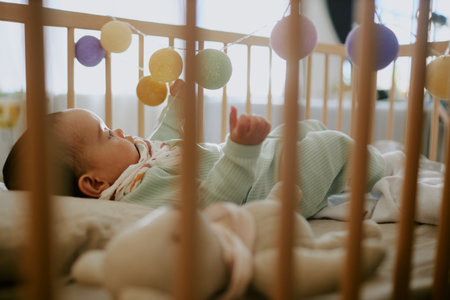 Little baby lying in cot and playing with rattle, he surrounded by plush toysの写真素材