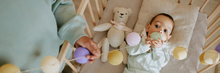 Website banner of baby boy playing with multicolored rattle and biting it white unrecognizable female hands adjusting rattleの写真素材