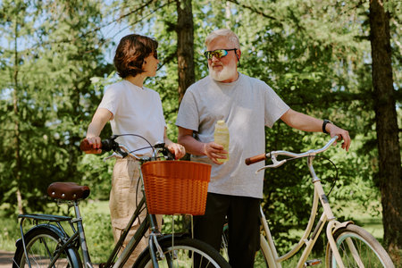 Senior husband offering bottle of water to his brunette wife after hours on retro bikesの写真素材