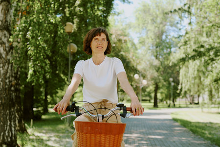 Brunette senior woman dressed in casual outfit riding retro bike in park aloneの写真素材