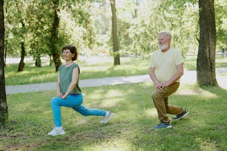Senior woman and man full of enthusiasms stretching their quads during open air training