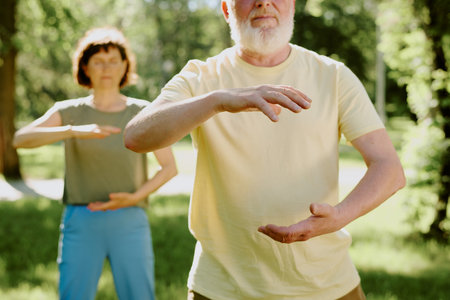 Unrecognizable old man holding his hand in air as part of static practice, senior brunette woman improving her karate skills in blurred backgroundの写真素材