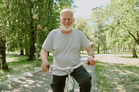 Portrait of smiling silver-haired man dressed in casual clothes, he having bike ride in parkの写真素材