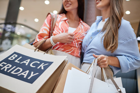 Medium close up of unrecognizable women holding black Friday paper bags while on escalatorの写真素材