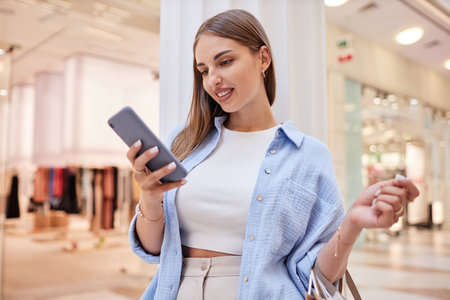 Young beautiful lady checking her phone during doing shopping in mallの写真素材