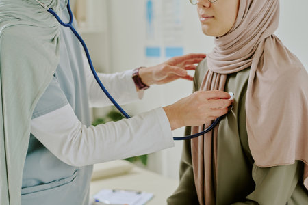 Medical professional wearing lab coat listening patients heartbeat using stethoscope in clinical setting, patient sitting still and allowing examinationの写真素材