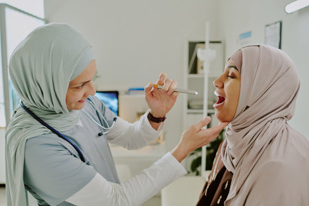Healthcare professional assisting patient by examining her throat, showcasing care and precision during medical consultationの写真素材