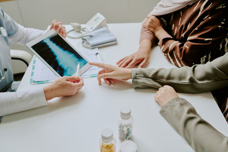 Medical professional showing x-ray results to patient in consultation room. Focus on discussing treatment options and diagnosis during appointmentの写真素材