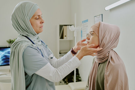Medical professional wearing scrubs, gently checking health of patient in clinic room Room equipped with medical tools and charts, patient wearing hijab and being attentiveの写真素材