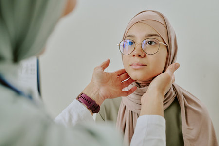 Medical professional closely examining young Muslim woman wearing hijab and glasses during health checkup in clinic setting. Woman appearing calm and attentive during examinationの写真素材