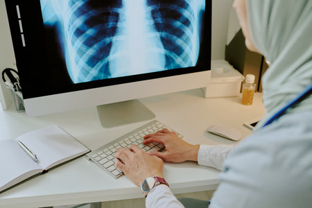 Medical professional analyzing chest x-ray on computer in modern office environment with minimal decor and professional equipment visible on deskの写真素材