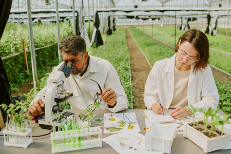 Scientists examining plant samples in modern greenhouse. Scene includes various laboratory equipment and plant specimens while researchers focus on conducting experimentsの写真素材