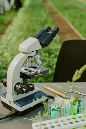 Microscope on table with botanical samples, focusing on scientific exploration and research in lab environment shown through laboratory equipment and green plants surrounding the workspaceの写真素材