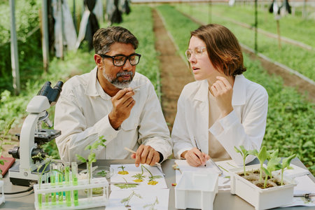 Scientists analyzing plant specimens in a laboratory setting with modern equipment, including microscope and test tubes, observing details and noting observationsの写真素材