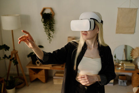 Medium shot of young Caucasian woman with albinism wearing headset standing in living room using virtual reality appの写真素材