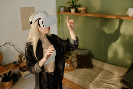 High angle view of young Caucasian woman with albinism wearing VR headset standing in living room playing modern video game or using appの写真素材