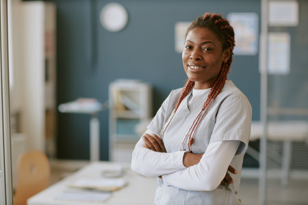 Portrait of confident female medical professional smiling with her arms crossed standing in hospital office setting with medical equipment in backgroundの写真素材