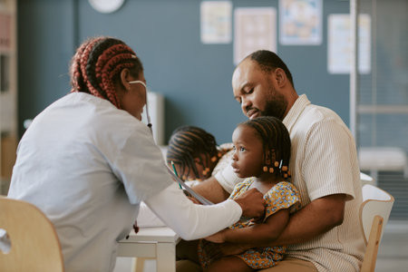 Nurse wearing white uniform examining young child with stethoscope held by father while sibling looking on sitting in office environmentの写真素材