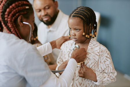 Child receiving medical examination with stethoscope by professional medical practitioner with other adults in background looking with concernの写真素材