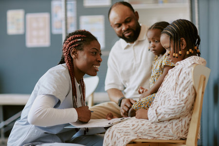Smiling healthcare worker engaging with a family in a medical setting, showing compassion and professionalism while two children and a parent observe attentivelyの写真素材
