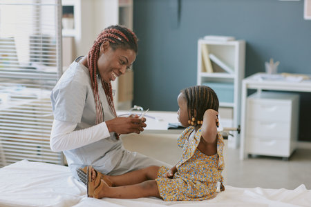 Smiling nurse wearing medical scrubs playing with young child on examination table in medical office, creating warm, comforting atmosphere for childの写真素材