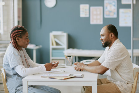 Nurse discussing healthcare plans with patient in medical office. Nurse holding pen and patient listening attentively, creating professional atmosphere focused on well-beingの写真素材