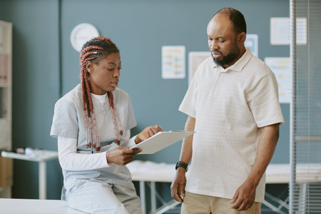 Health professional showing medical report in clinic, discussed with patient appearing concerned. Both involved in understanding medical details during consultationの写真素材