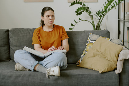 Young serious woman reading Braille book while spending time at homeの写真素材