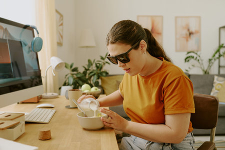 Young woman with disability adding whole milk in bowl with flakesの写真素材