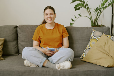 Happy woman with disability resting on comfortable sofa, smiling widely and holding smartphoneの写真素材