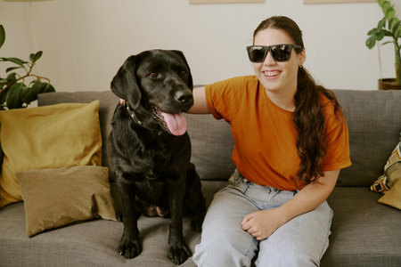 Smiling young Caucasian blind woman with sunglasses smiling widely and petting her loyal friendの写真素材