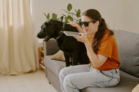 Happy woman with disability petting her black Labrador while speaking on smartphoneの写真素材
