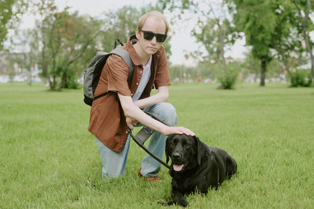 Portrait of Caucasian man with disability petting his black Labrador while he lying on grassの写真素材