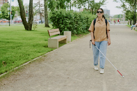Independent woman with disability walking in summer park with help of caneの写真素材