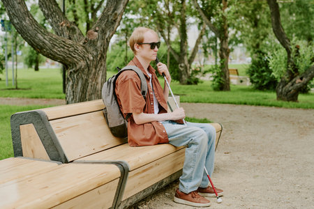 Caucasian man with disability holding metal stick while sitting on wooden bench in parkの写真素材