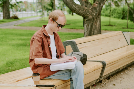 Side view shot of Caucasian man with disability reading Braille book in park while enjoying fresh air and summer dayの写真素材