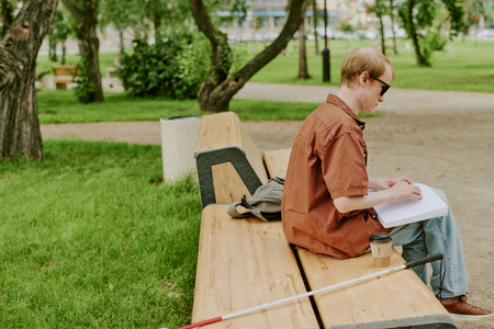 Unrecognizable man sitting on wooden bench and enjoying Braille book in parkの写真素材