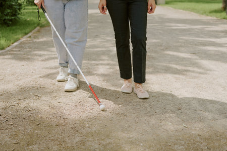 Unrecognizable friends walking in park, person with disability using meta cane to orientate while walkingの写真素材