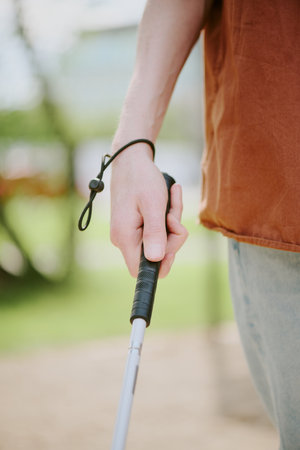 Vertical medium close up shot of unrecognizable male hand holding metal cane to walk in parkの写真素材