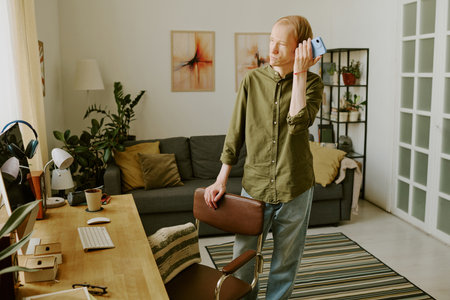 Man with disability listening to audio while standing next to workspaces in living room