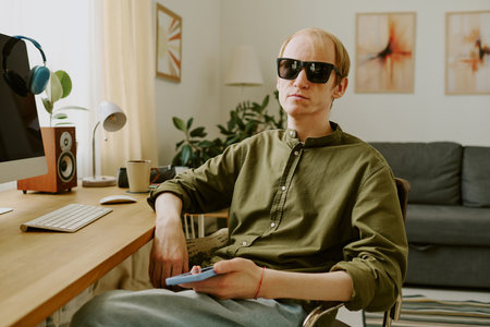 Caucasian man with disability wearing black sunglasses and posing for portrait in cozy living room with work zoneの写真素材