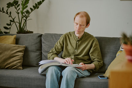 Caucasian man with disability enjoying reading Braille book while staying at homeの写真素材