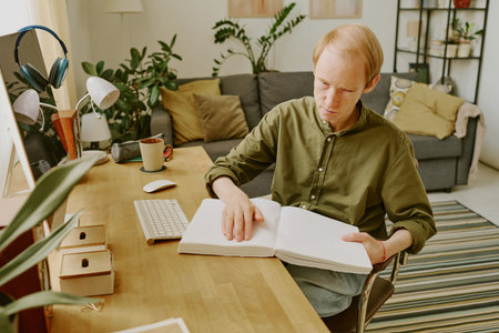 Caucasian man with disability reading Braille book while spending day off at homeの写真素材