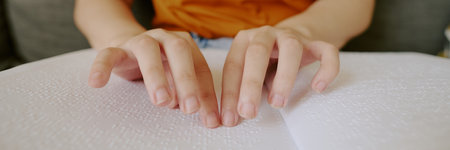 Website header of pale female hands reading Braille writing system on book pageの写真素材