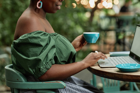 Side view shot of unrecognizable woman typing on keyboard while holding coffee cupの写真素材