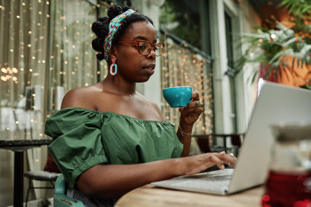 Young African American woman drinking hot black tea while checking social networksの写真素材